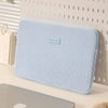 Una funda protectora delgada azul claro para una laptop apoyada sobre una superficie blanca.