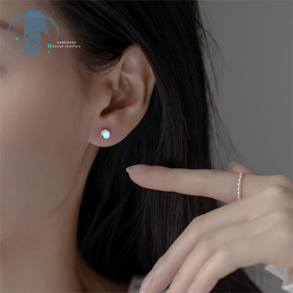Close-up of a woman's ear showing minimalist moonstone stud earrings and a hand wearing a simple ring.