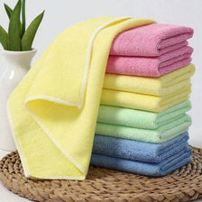 A stack of brightly colored microfiber cleaning cloths in yellow, pink, and green resting on a woven mat.