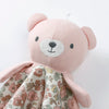 A pink stuffed animal with a light gray face and floral patterned fabric underneath.