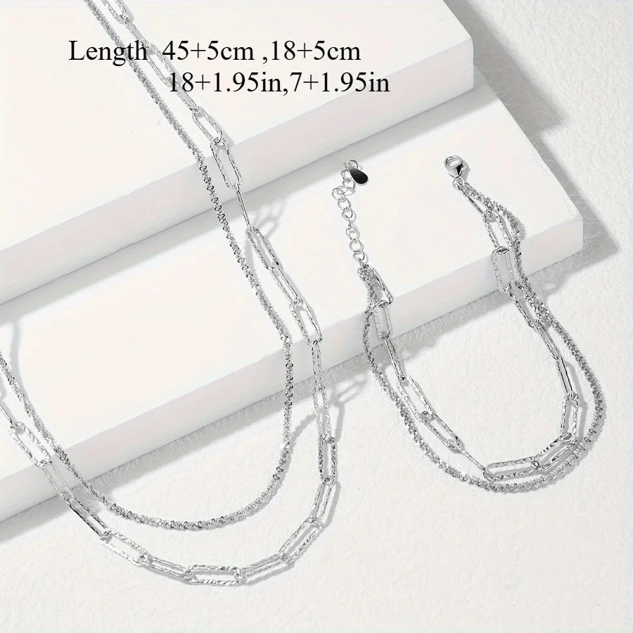 A set of sterling silver paperclip chain necklaces and bracelets displayed on a white surface.