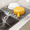 A silicone dish drying mat is shown with a yellow bowl and utensils on it, draining water into a tray.
