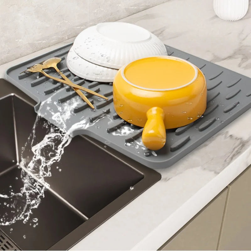 A silicone dish drying mat is shown with a yellow bowl and utensils on it, draining water into a tray.