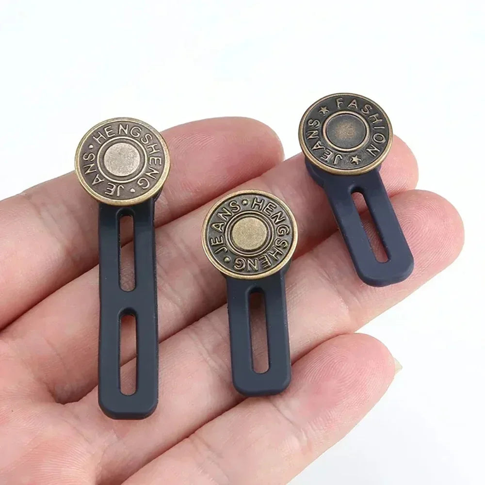 Une main tient trois gaines réglables dorées pour jeans et pantalons.