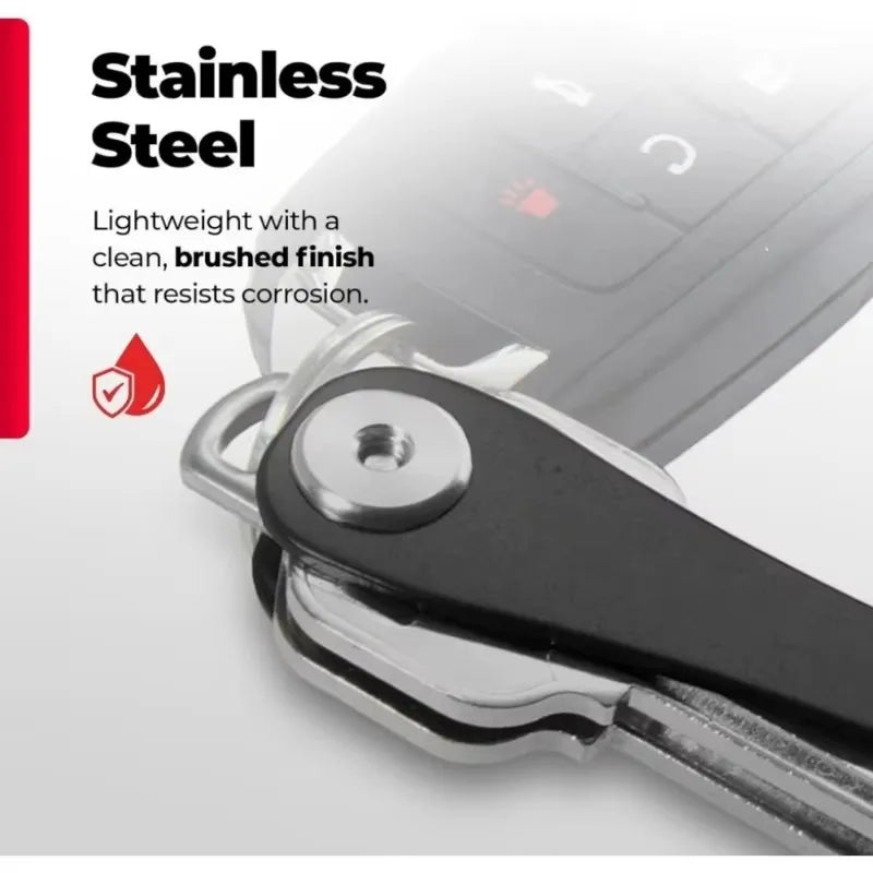 A close-up of a stainless steel key clip with a carabiner hook attached to a dark surface.