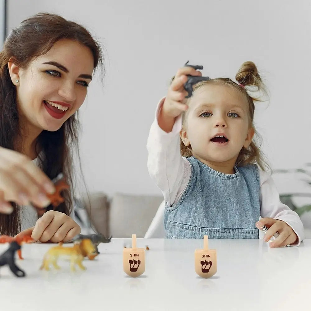 A woman and a child are shown playing with wooden spinning tops on a table.