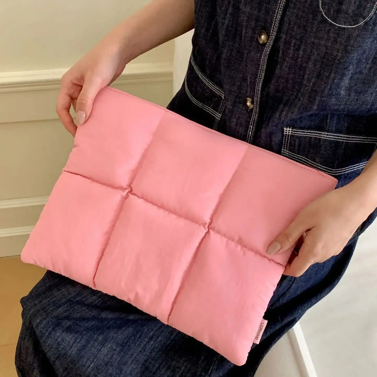 Person hält eine gepolsterte, pinke Laptoptasche mit Reißverschluss.
