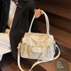 A white soft leather plaid crossbody bag with adjustable strap is held by a person in a dark suit jacket.
