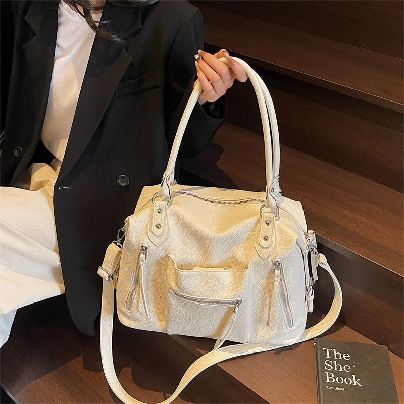 A white soft leather plaid crossbody bag with adjustable strap is held by a person in a dark suit jacket.