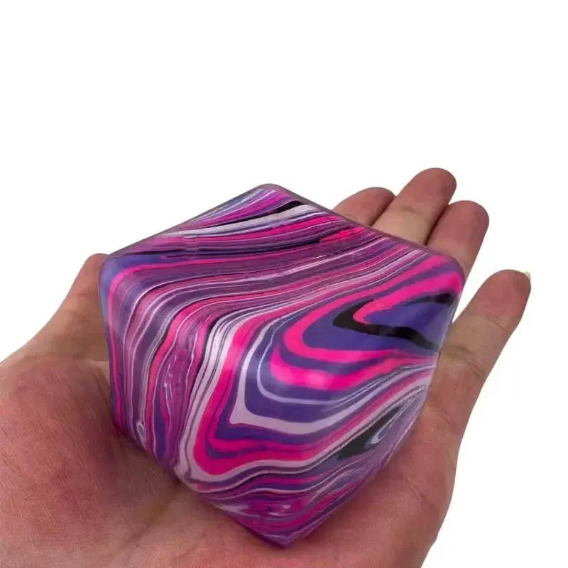 Une main tient un cube de jeu en gel apaisant violet et rose marbré et brillant.