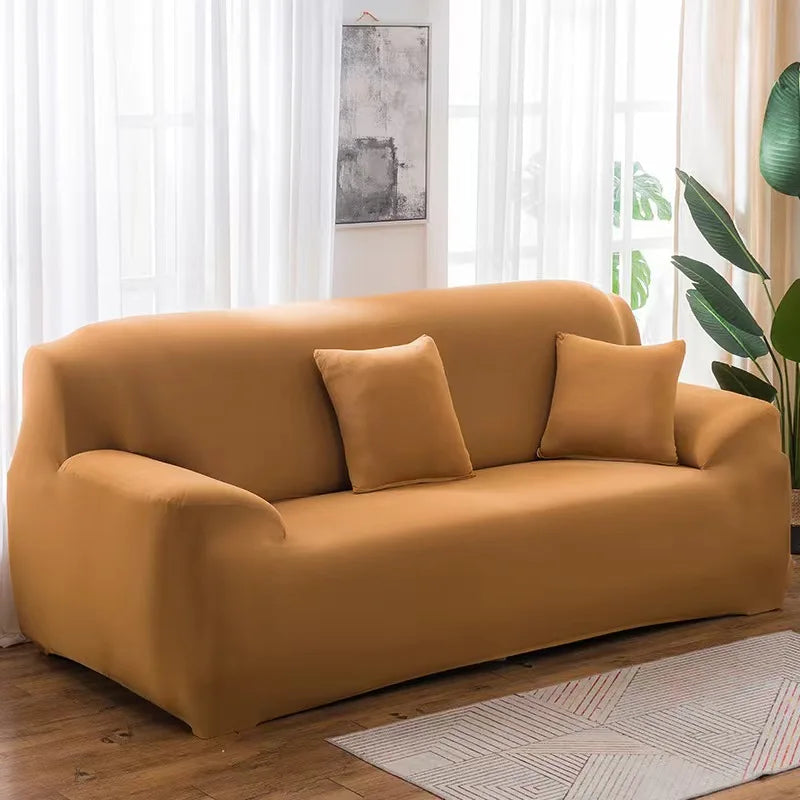 A mustard yellow elastic stretch sofa cover for a 3-seater sofa with two accent pillows, set in a bright room.