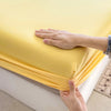 A hand is touching a bright yellow fitted sheet, showing the fabric texture and elastic band.