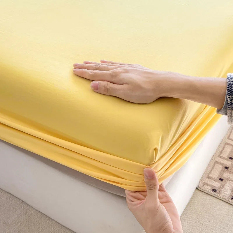 A hand is touching a bright yellow fitted sheet, showing the fabric texture and elastic band.