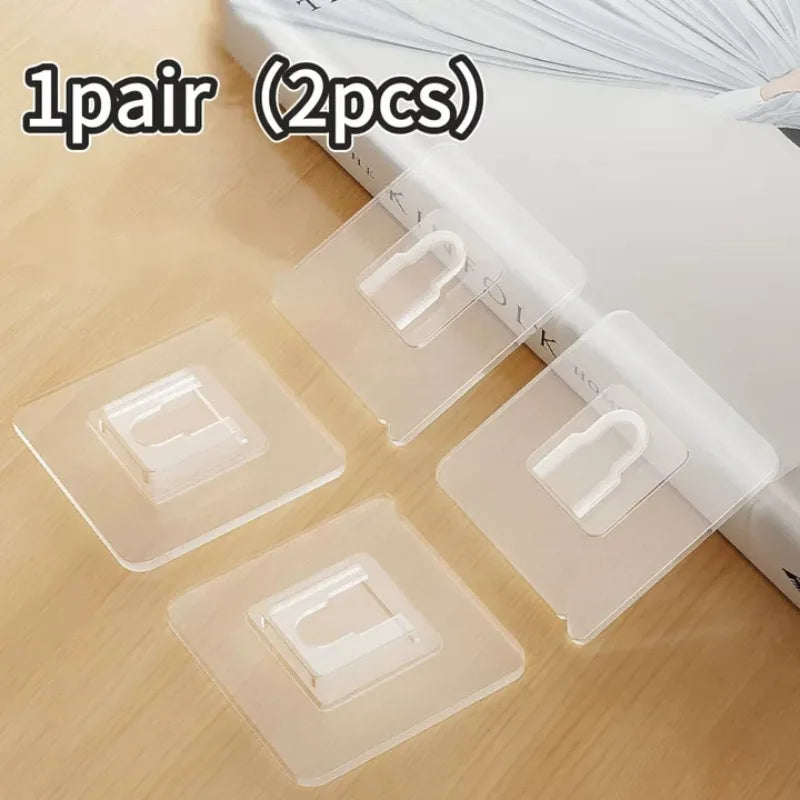 A pair of transparent, double-sided adhesive wall hooks are shown on a wooden surface.