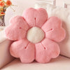 A pink plush daisy flower throw pillow with a white center resting on a light-colored sofa.