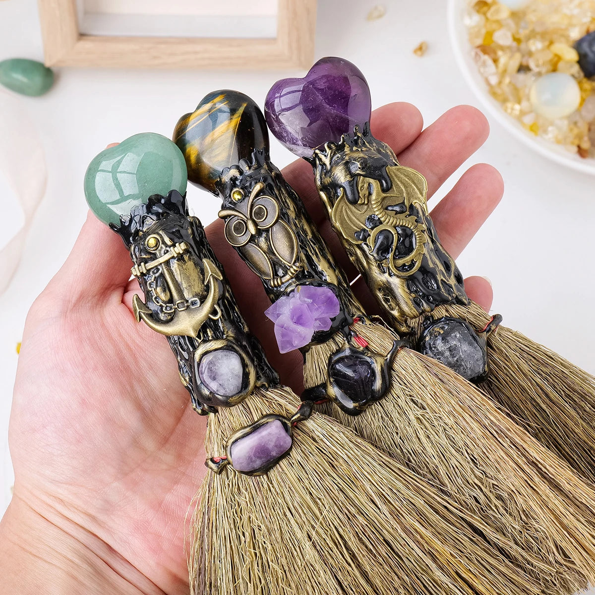 Una mano sostiene una escoba de corazón de cristal natural hecha con cristales de varios colores como verde y púrpura.