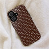 A brown patterned phone case with white polka dots resting on a fluffy beige surface.