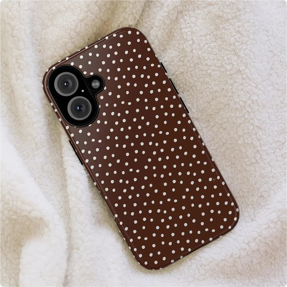 A brown patterned phone case with white polka dots resting on a fluffy beige surface.