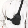 A black compact canvas crossbody sling bag is attached to the front of a white jacket.