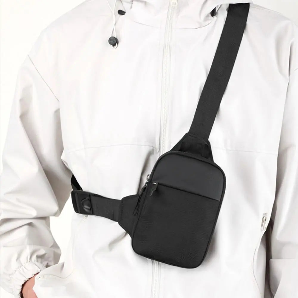 A black compact canvas crossbody sling bag is attached to the front of a white jacket.