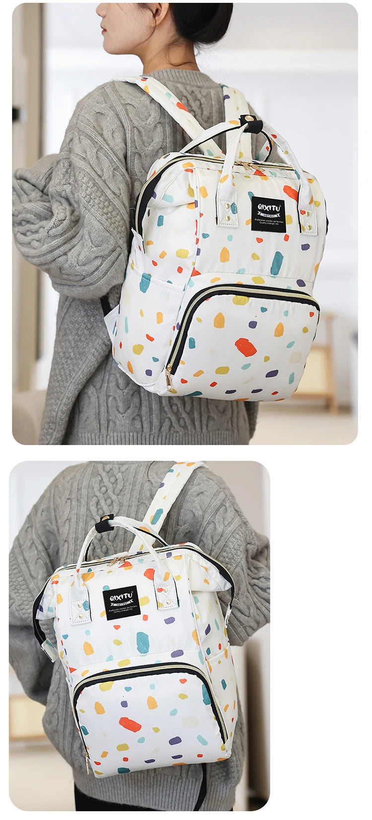 A woman is wearing a white and multi-colored patterned backpack diaper bag with black accents over a gray sweater.
