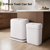 A set of two white, slim rectangular trash cans with lids sitting on a wooden cabinet top.