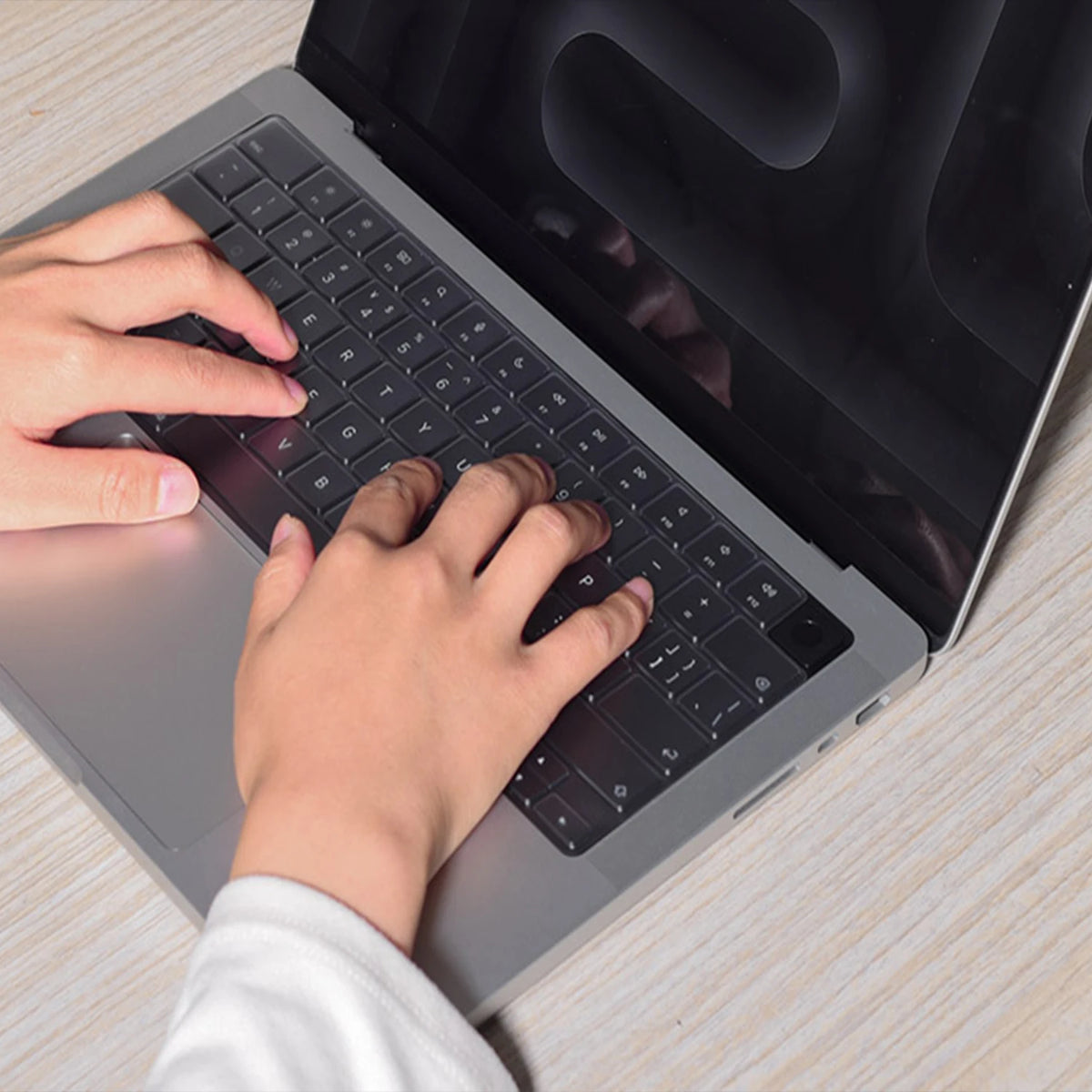 A person's hands are typing on a silver laptop keyboard with a silicone keyboard cover.