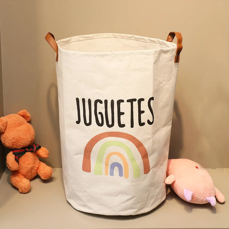 A white fabric storage basket with a rainbow design and the word JUGUETES printed on it.
