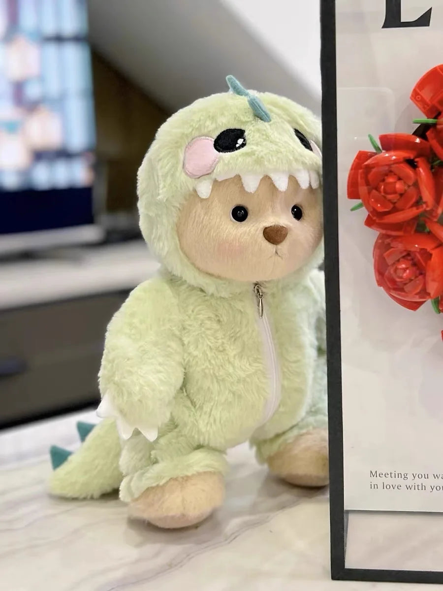 A soft, light green teddy bear doll dressed in a dinosaur jumpsuit outfit.
