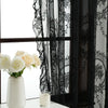 Black and white lace sheer curtains with floral embroidery hanging in a window next to a white vase of roses
