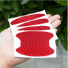 A hand holds a white card displaying three red carbon fiber patterns, representing door handle protector film.