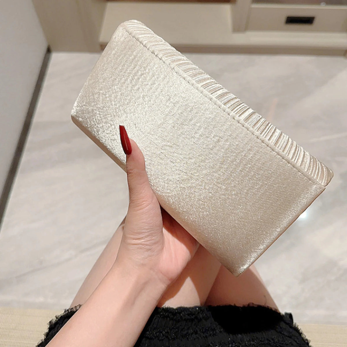 A hand holds an elegant patent leather clutch bag with a chain strap in a light beige color.