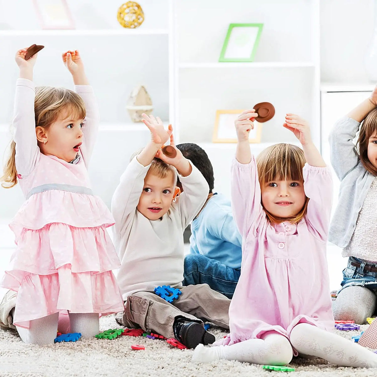 Three young children are holding miniature cowboy hats in a bright indoor setting.