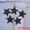A set of five black glitter star iron-on embroidered patches on a light blue denim fabric.