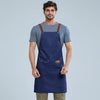 A man wearing a navy blue waterproof adjustable kitchen apron over a gray t-shirt.
