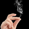 A hand is blowing a plume of white smoke from a piece of chemical smoke magic paper against a black background.