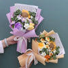 Handgemachter Blumenstrauß aus Häkelarbeit mit Sonnenblumen, in rosa Papier eingewickelt und mit cremefarbigem Band gebunden.