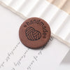 A round, brown felt label with a stitched heart design placed on a white paper background.