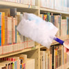 A hand is using a white microfiber duster to clean books and surfaces on a shelf in a library or study.