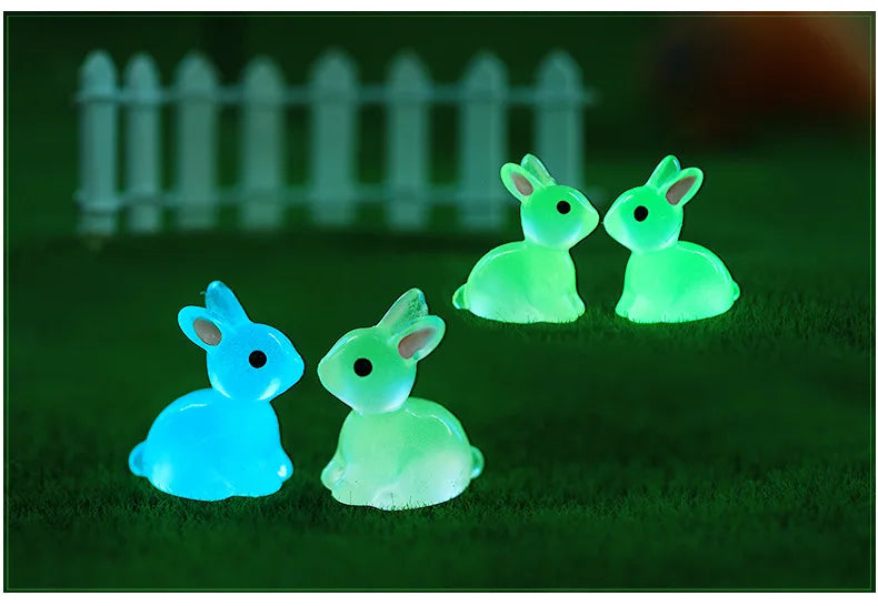 A set of three glowing resin miniature bunny figurines in shades of light green and blue on a dark green surface.