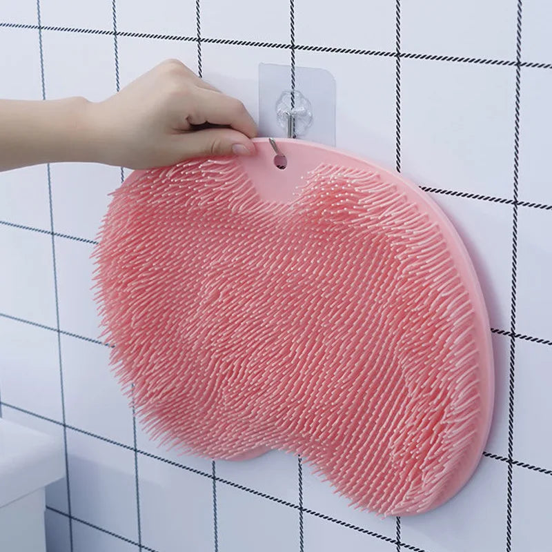 A hand is placing a pink suction cup foot massage mat with exfoliating bristles onto a white tiled wall.