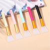 A set of five silicone facial mask brushes in various pastel colors, including pink, blue, and yellow, resting on a light bac