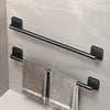 A black wall-mounted towel rack with a horizontal bar and two hanging gray towels mounted on a light gray wall.