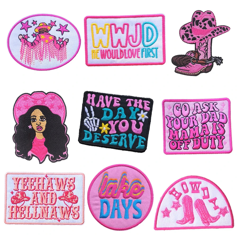 A collection of pink and black embroidered letter patches featuring phrases like WWJD, Have the Day You Deserve, and Lake Day