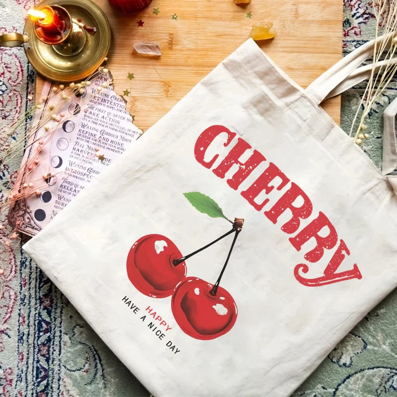 A white canvas tote bag with red cherry print and text on a wooden surface.