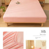 A pink fitted sheet is displayed on a wooden bed frame with soft fabric and elastic edges.