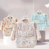 A light floral patterned children's waterproof long sleeve feeding bib with a catch pocket displayed on a hanger.