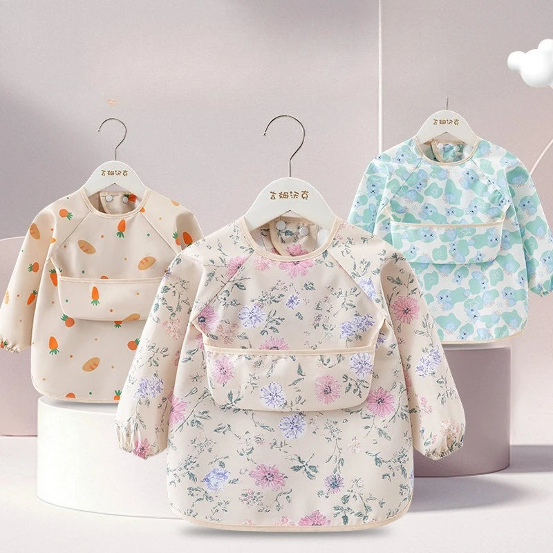 A light floral patterned children's waterproof long sleeve feeding bib with a catch pocket displayed on a hanger.