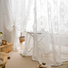 White sheer curtains with floral embroidery draped in a romantic style over a table.