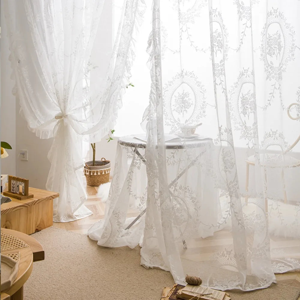 White sheer curtains with floral embroidery draped in a romantic style over a table.